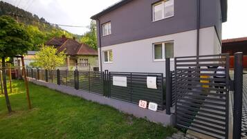 A modern two-story house with a grey exterior, a fenced yard, and a small garden area.