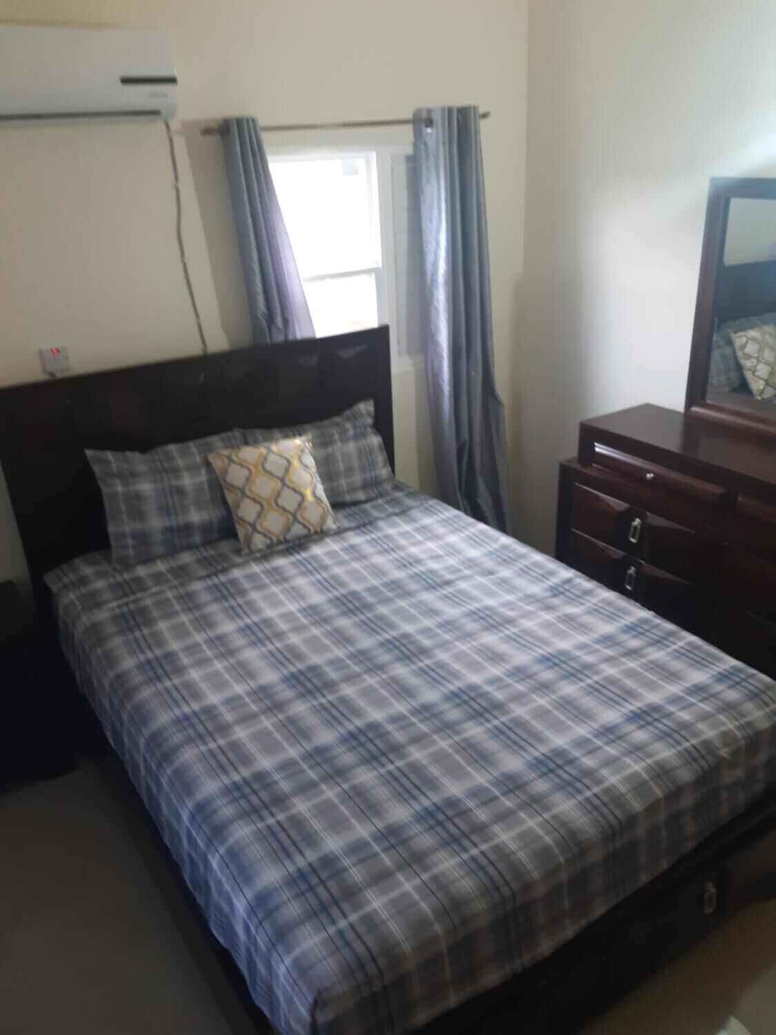 Una cama con colcha a cuadros, cabecera de madera y mesita de noche con espejo.