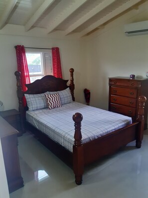 Une chambre à coucher avec un lit en bois, une commode et une fenêtre ornée de rideaux rouges.