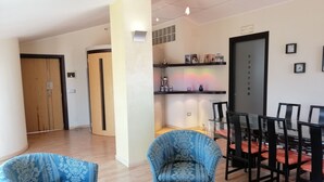 Un salon moderne avec un coin repas, comprenant un canapé, des fauteuils, une table et une bibliothèque remplie de livres et d’objets décoratifs.