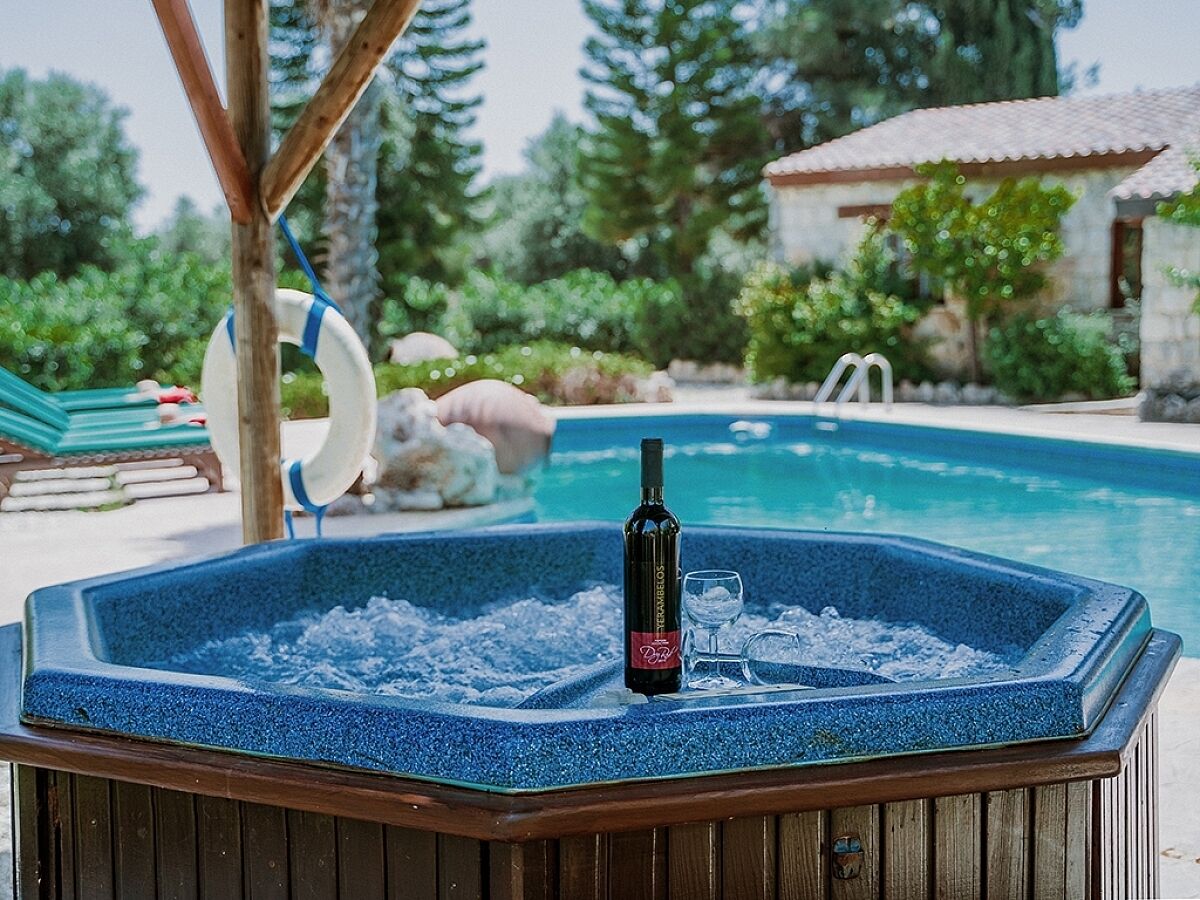 Un jacuzzi con una botella de vino y copas, rodeado por una piscina y follaje.