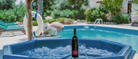 A hot tub with a bottle of wine and glasses, surrounded by a pool and greenery.