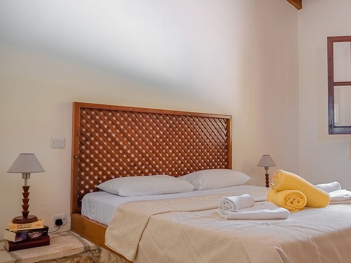 A neatly made bed with white linens and a wooden headboard with a lattice pattern. There are two bedside lamps and a stack of books on the nightstand.