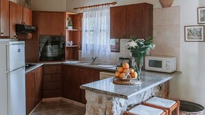 A kitchen with wooden cabinets, a granite countertop, a refrigerator, an oven, a sink, a microwave, and a vase with flowers. - Spacious Villa, Large Private Pool, Outdoor Jacuzzi, Attractive Gardens, 10 min walk to the Beach! (Latchi)