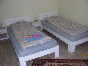 Two single beds with white frames and grey mattresses, each with a knitted blanket and folded towels. - Small holiday apartment next to Fulda Rhön Vogelsberg good central location Hesse up to 2 persons (Künzell)