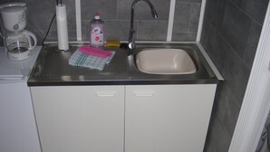 Una cocina con un lavamanos, una cafetera, una botella de detergente y una esponja.