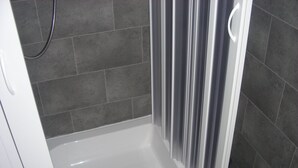 Zona de ducha con bañera blanca, azulejos grises oscuros y cortina de ducha.
