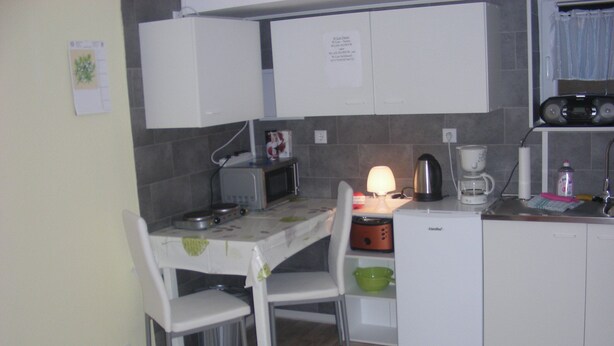 Una cocina compacta con armarios blancos, un microondas, una cafetera y una mesa con sillas.