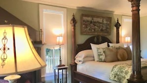 Een slaapkamer met een hemelbed, nachtkastje, lamp en een schilderij aan de muur.