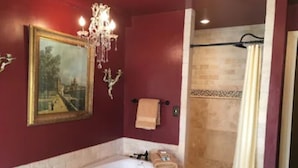 Een badkamer met een bad, een douche, een kroonluchter en een gekaderd schilderij aan de muur.