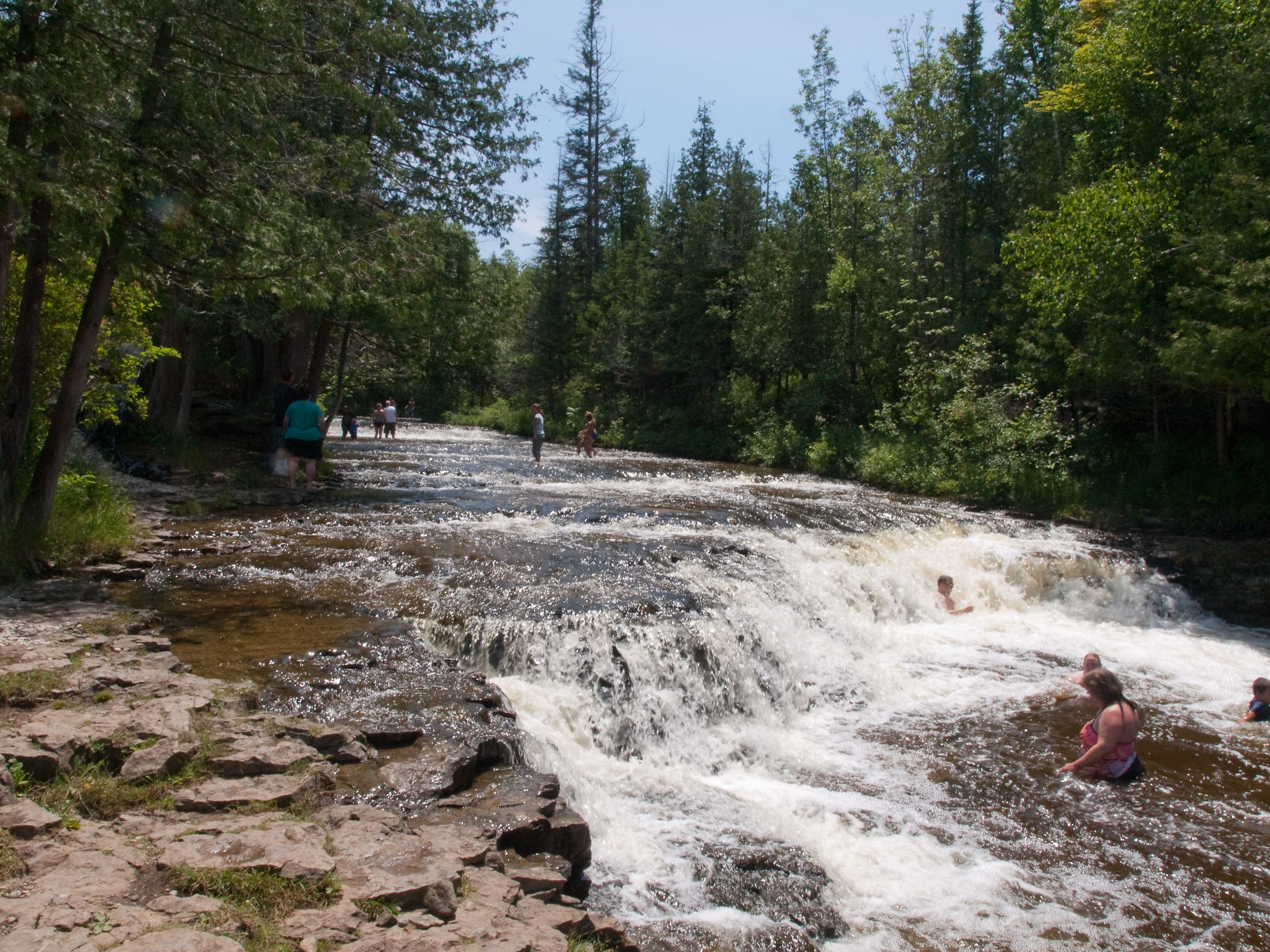 A waterfall in a forested area with people enjoying the water.