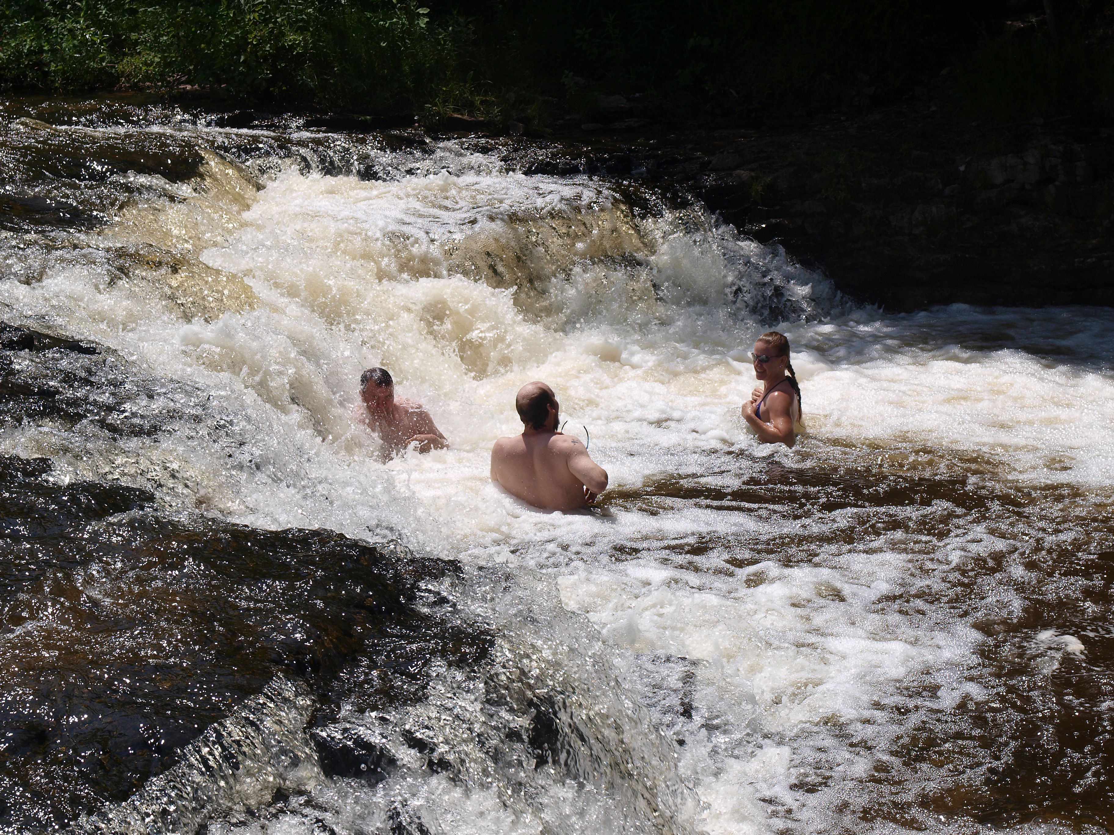 Tre persone in un ambiente acquatico naturale, forse un fiume o una cascata.