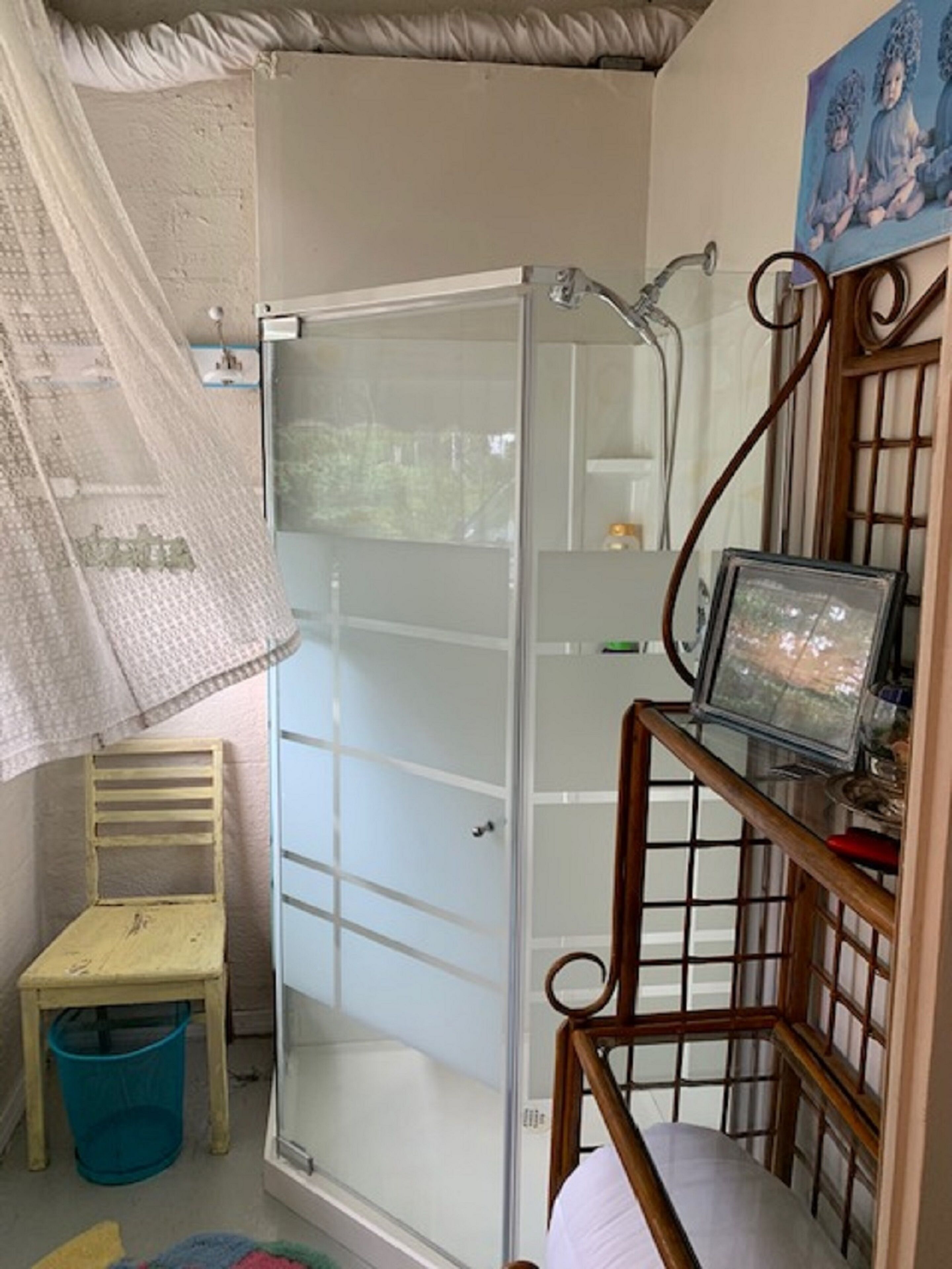 A shower with a glass door, a wooden chair, a small table, and a picture frame on a shelf.