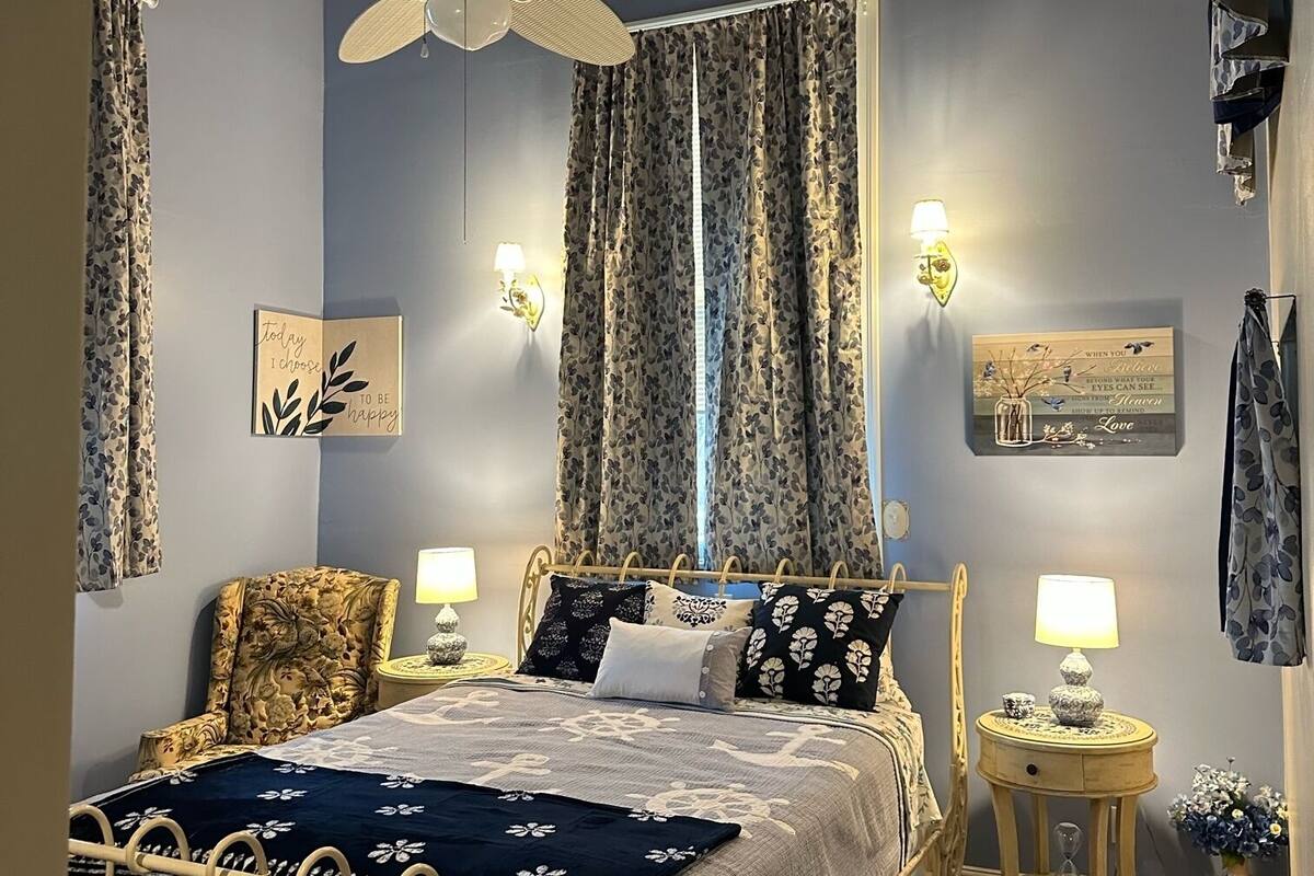 A bedroom with a bed, a chair, a ceiling fan, and decorative wall lights.