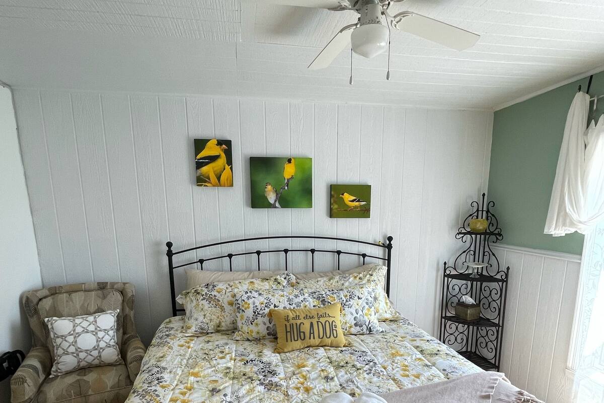 A bedroom with a bed, a chair, a ceiling fan, and wall art.