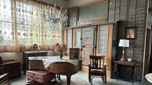 A vintage room with a wooden desk, a chair, a vintage lamp, and a large window with patterned curtains. - The Purple Martin Inn (Rogers City)