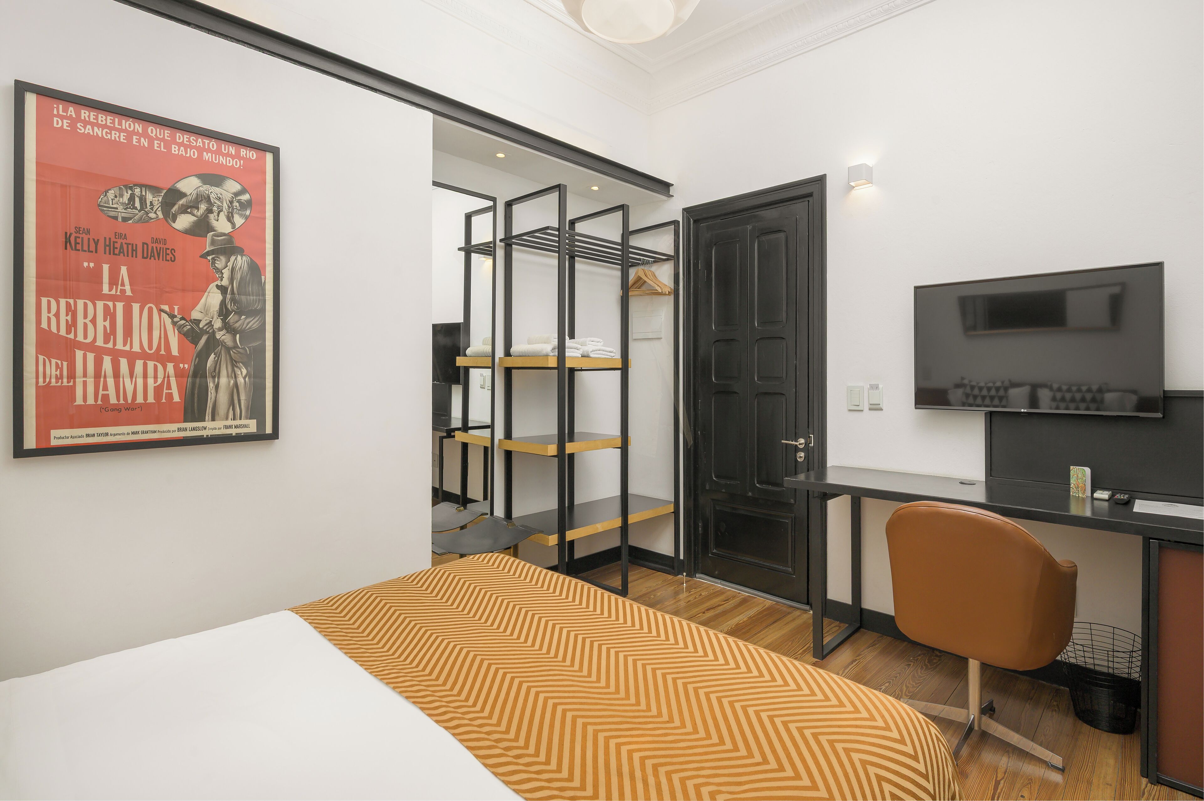 Un dormitorio con cama, escritorio, silla, televisor y armario con estantes.