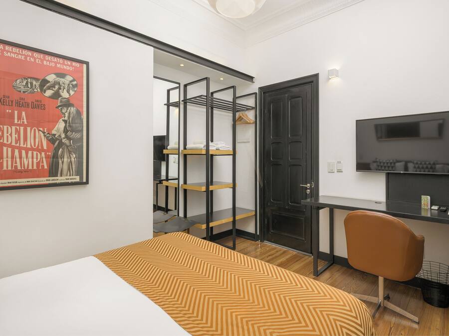 Un dormitorio con cama, escritorio, silla, televisor y armario con estantes.