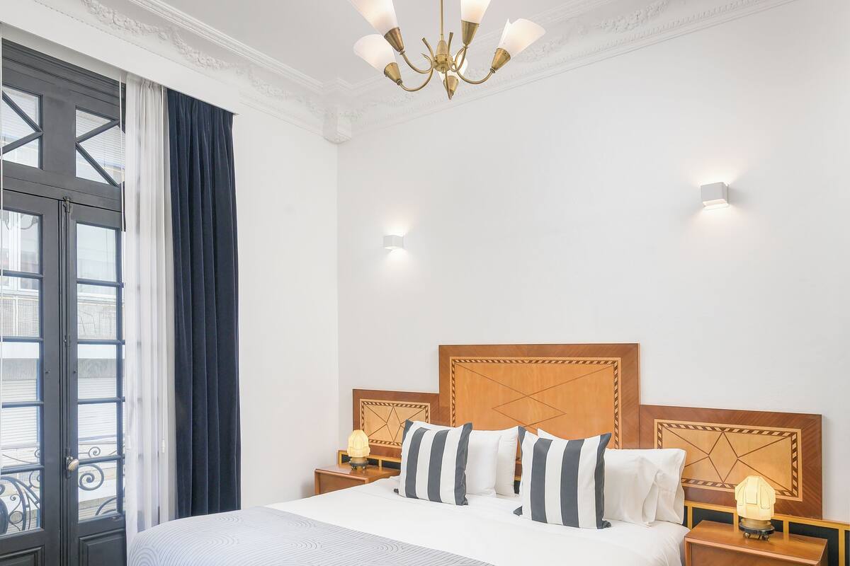 Una habitación de hotel con una cama grande, cabecera de madera, lámparas de noche y un candelabro.