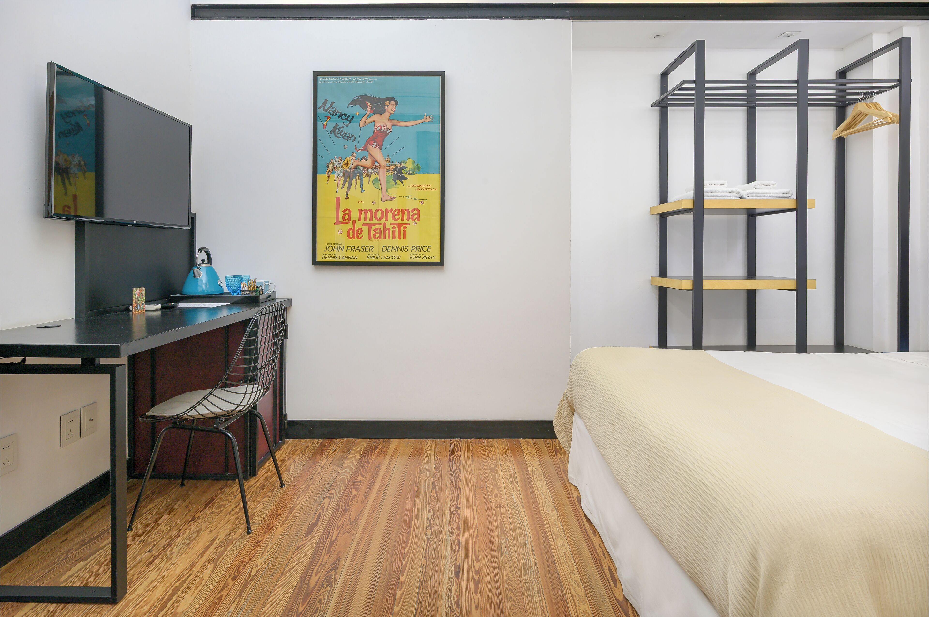 A hotel room with a bed, a desk with a chair, a TV mounted on the wall, and a poster on the wall.