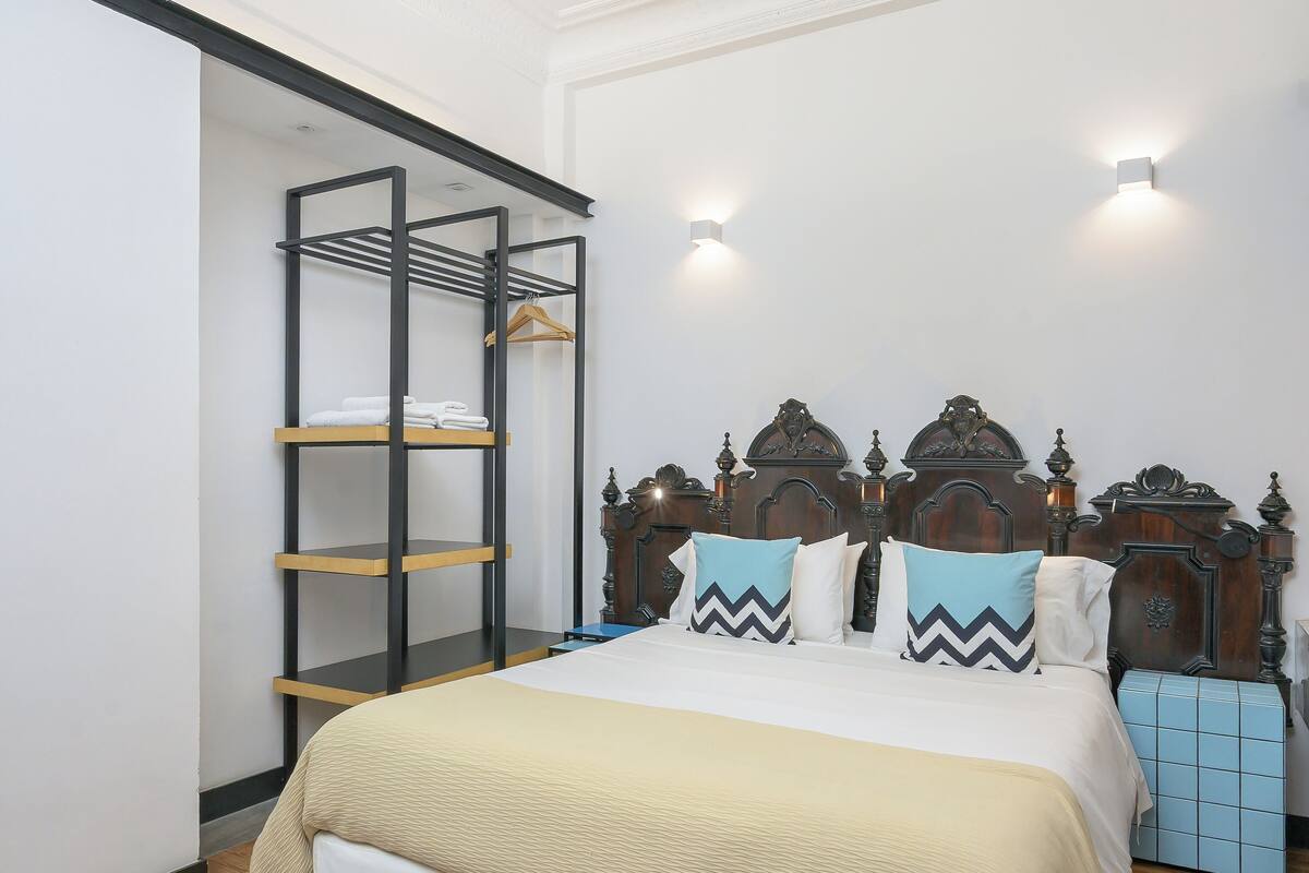 Un dormitorio con una cama de madera, una estantería de metal negro y un baúl azul.