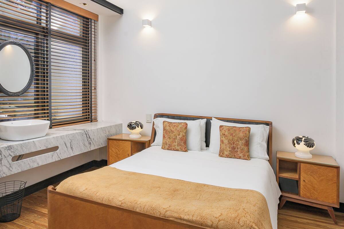 Un dormitorio moderno con una cama grande, un tocador de mármol y piso de madera.