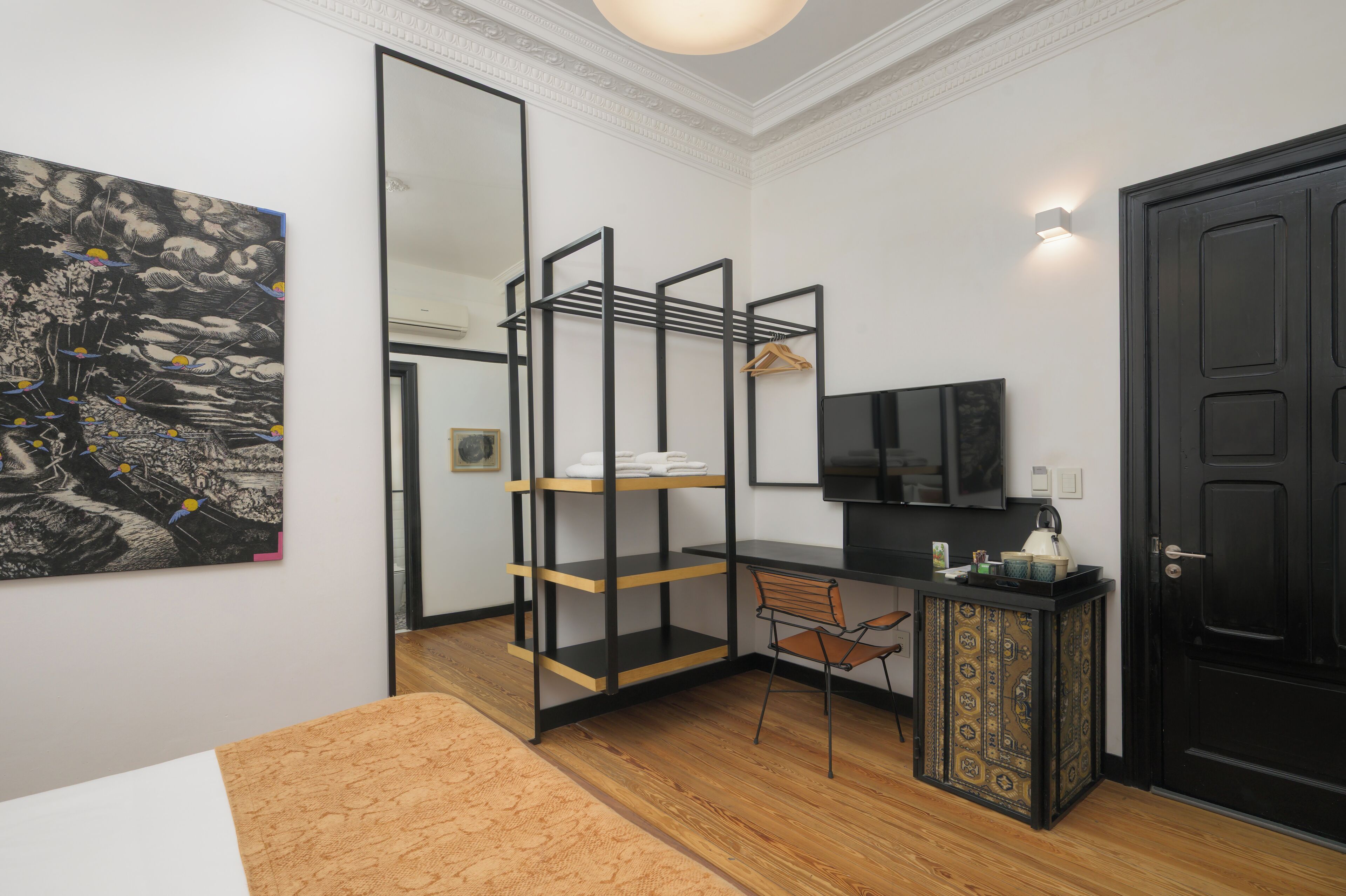 Una habitación con una cama, un escritorio con silla, un armario negro, una puerta negra y una obra de arte grande enmarcada en la pared.