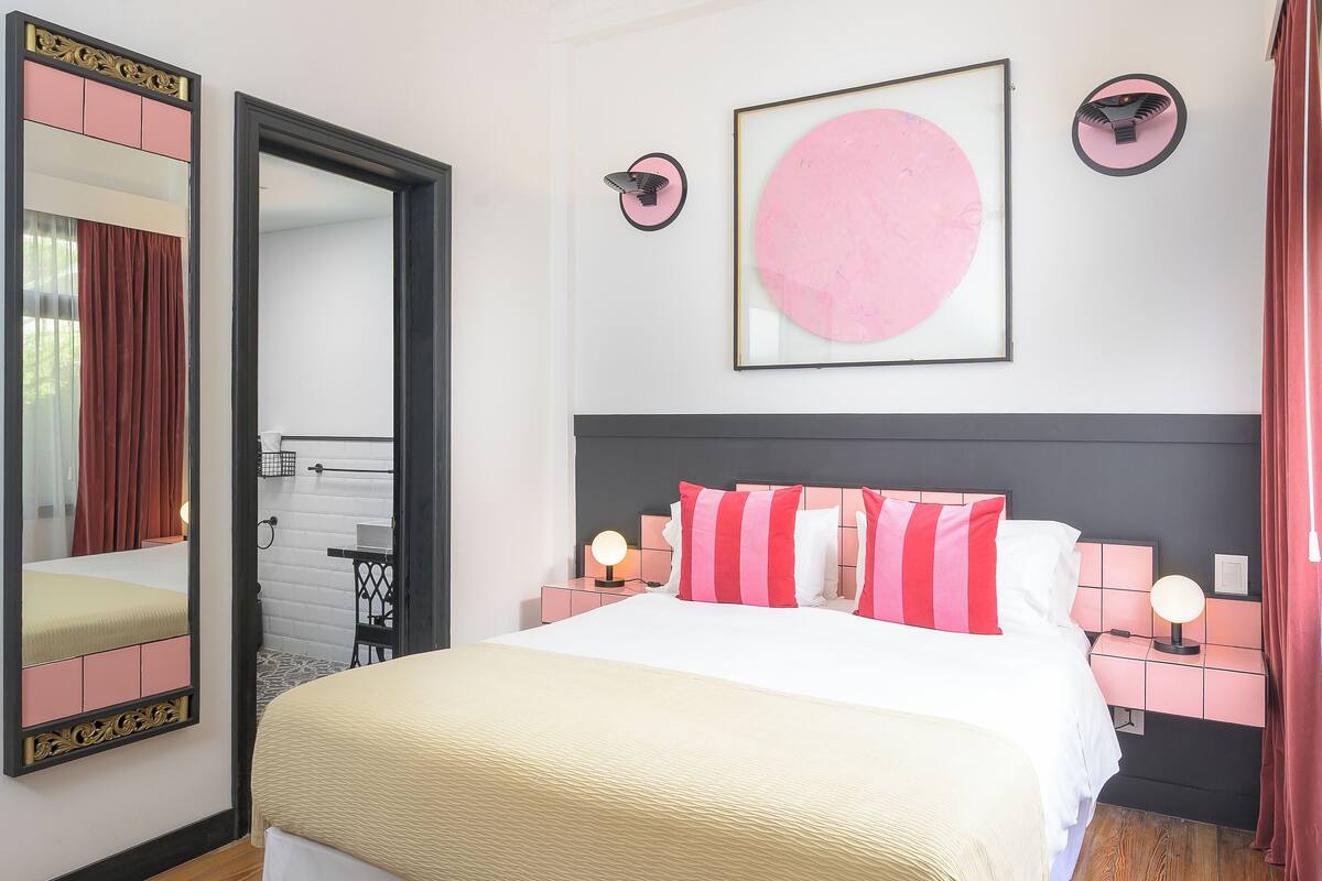 Un dormitorio moderno con una cama grande, mesitas de noche con lámparas, un ventilador de techo y un espejo amplio.