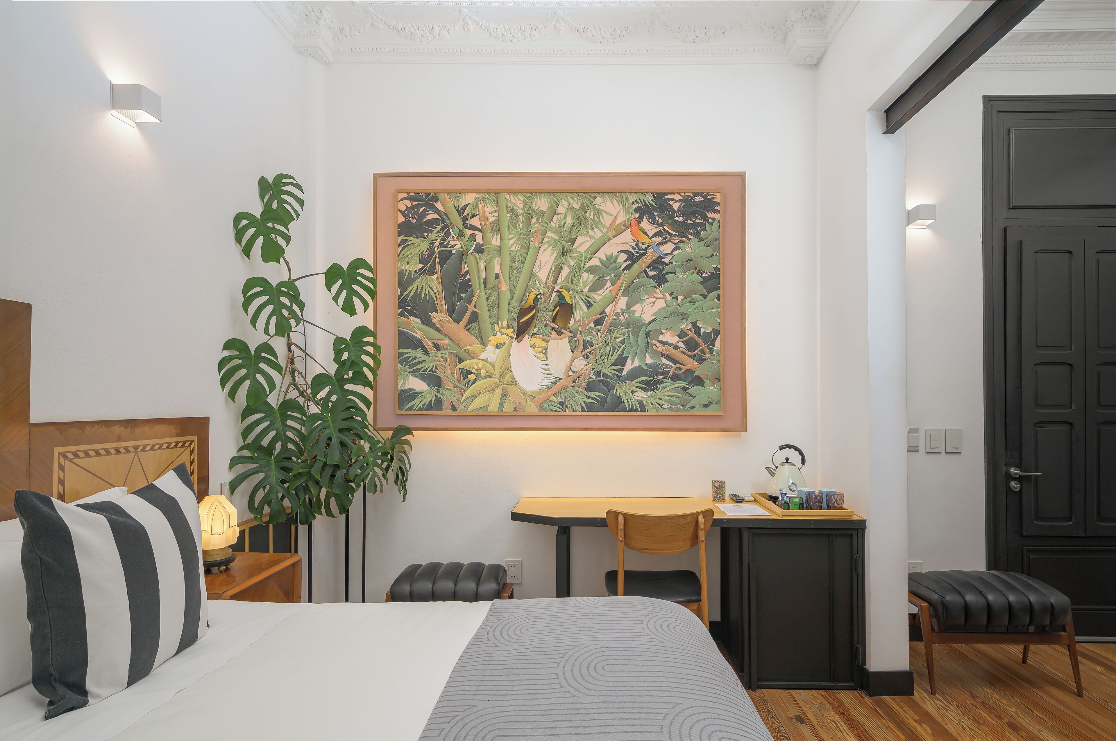 Hotellihuone, jossa on sänky, työpöytä, tuoli, pieni pöytä, ruukkukasvi ja ovi.
