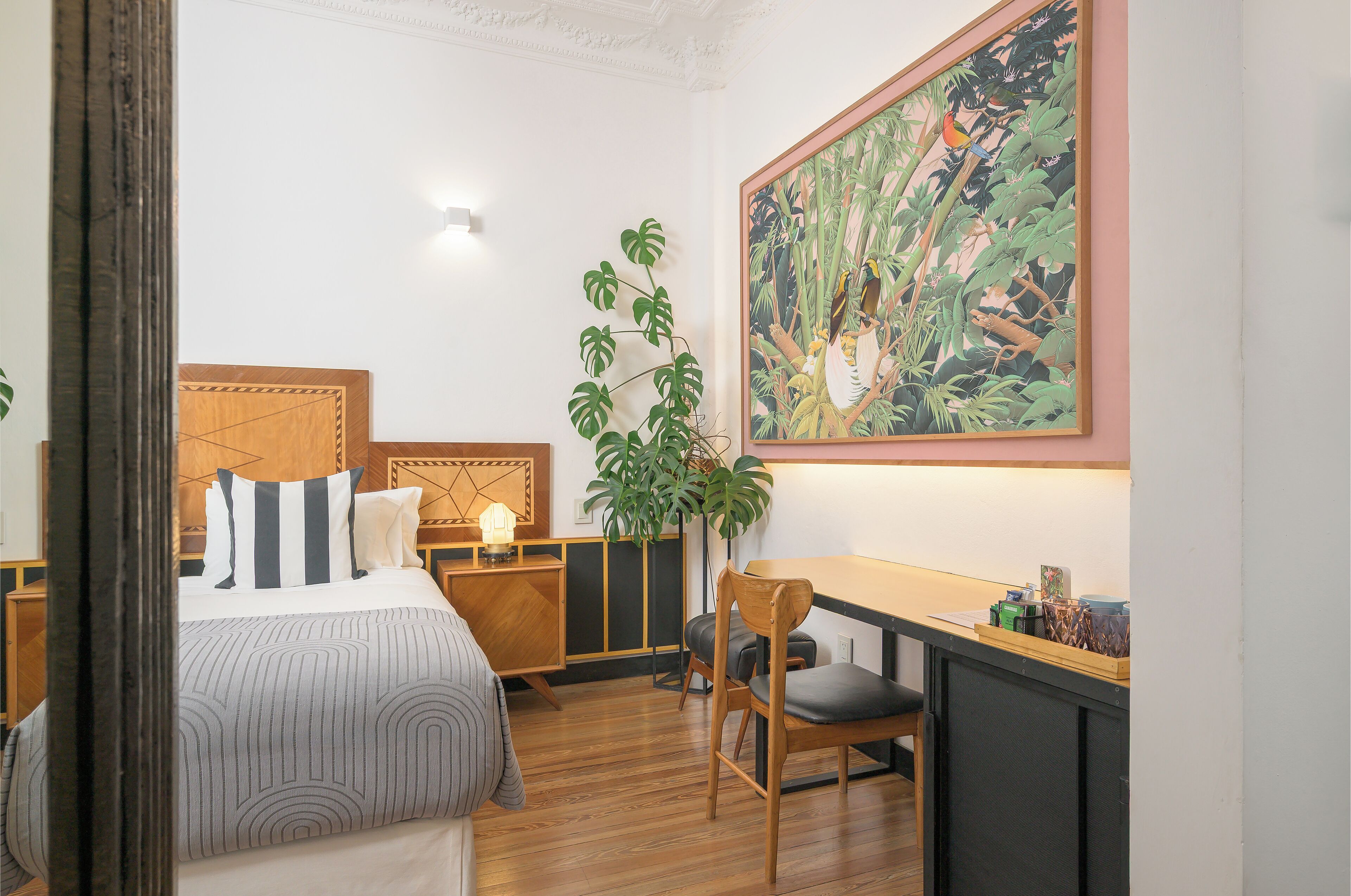 Habitación de hotel con cama, mesita de noche, silla, escritorio y un cuadro grande en la pared.