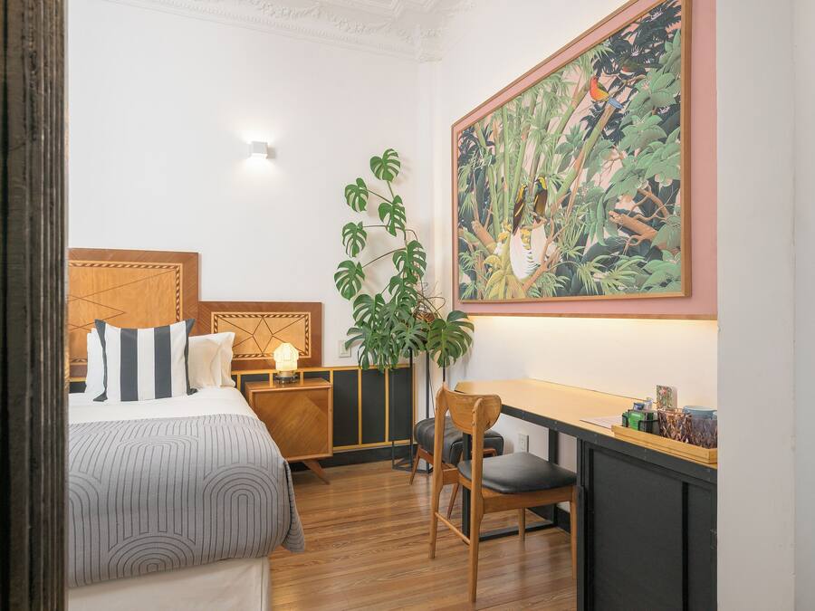 Habitación de hotel con cama, mesita de noche, silla, escritorio y un cuadro grande en la pared.