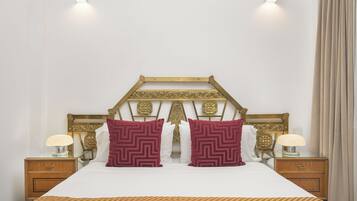 Una cama bien hecha con una colcha estampada, dos almohadones decorativos, un cabecero de madera con intrincados grabados y lámparas de noche sobre mesitas de madera.