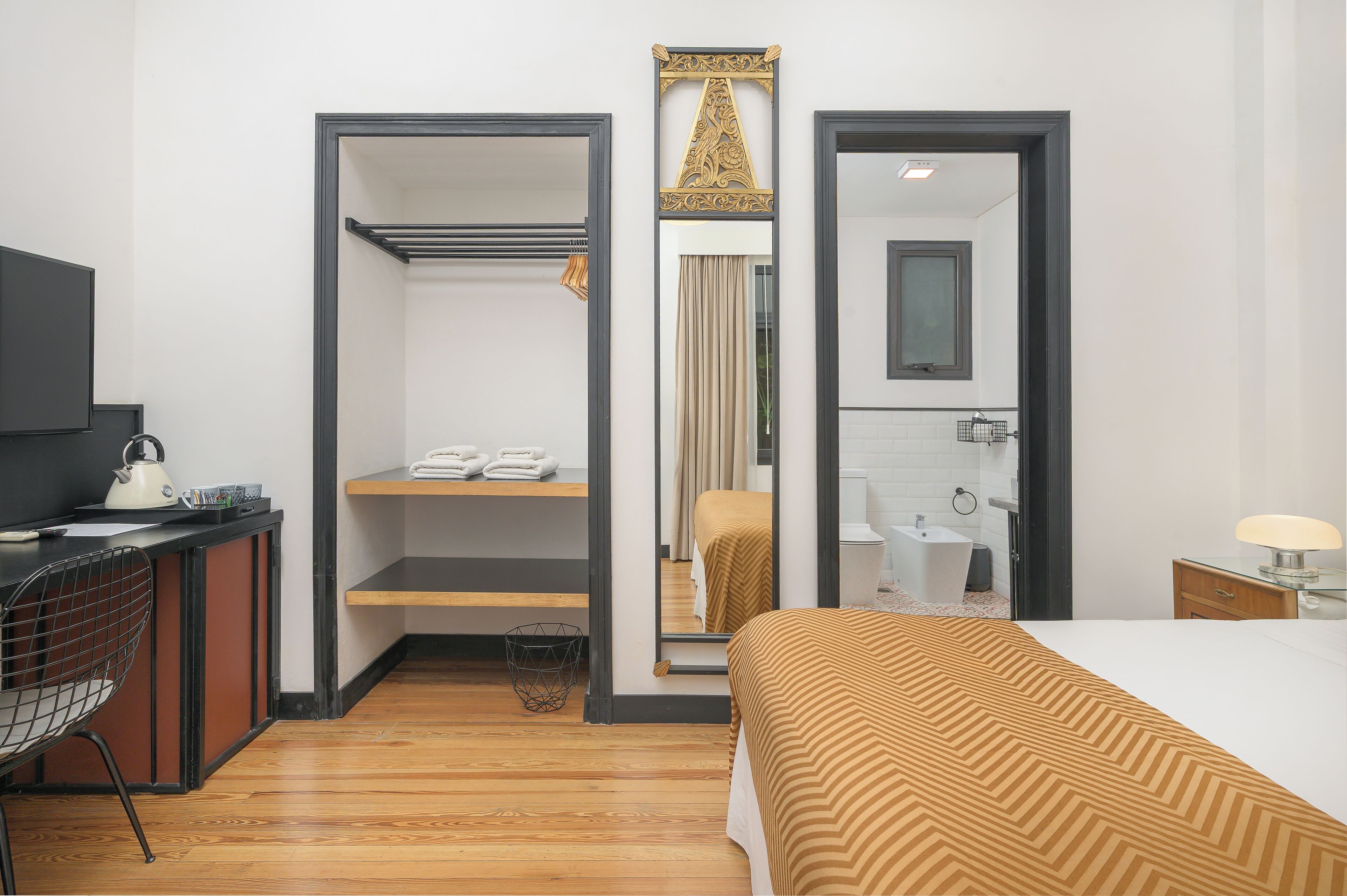 Habitación de hotel con cama, escritorio con silla, espejo, lavabo y zona de ducha.