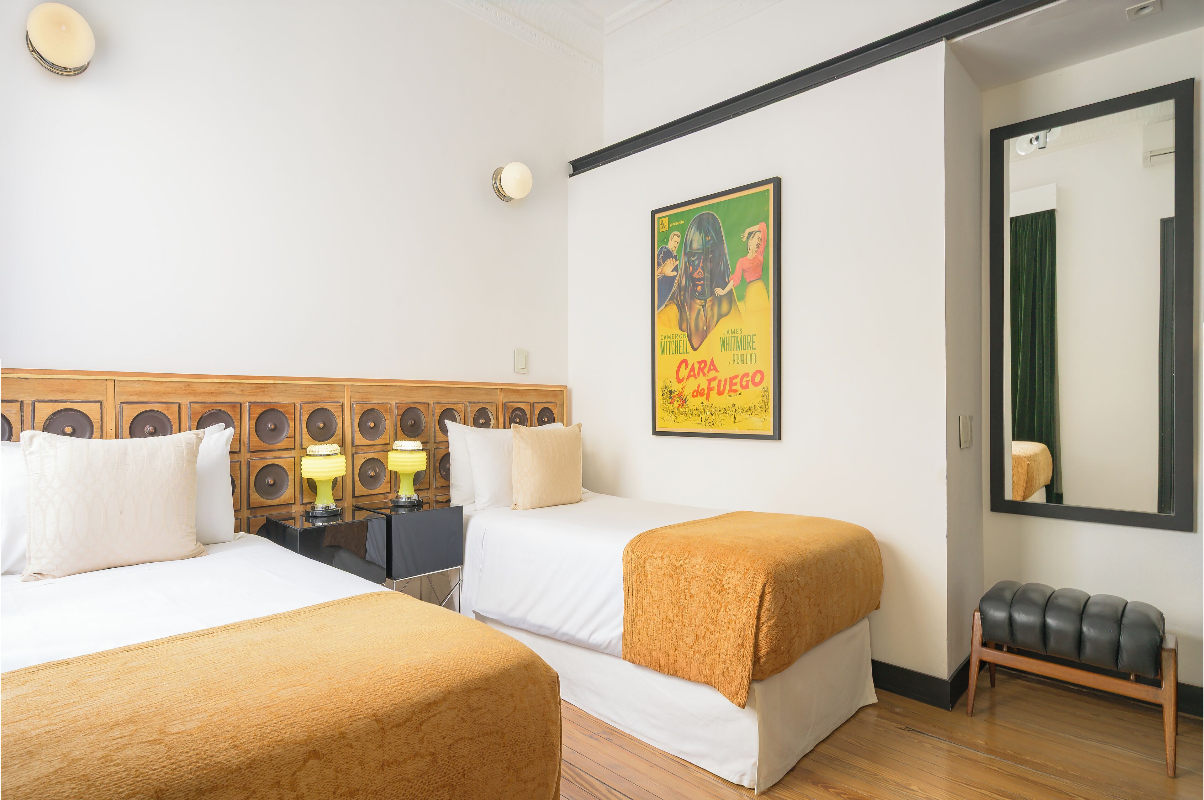Habitación de hotel con dos camas, un banco, un espejo, un cartel y una lámpara.
