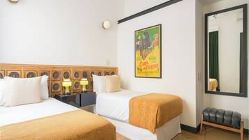 Habitación de hotel con dos camas, un banco, un espejo, un cartel y una lámpara.