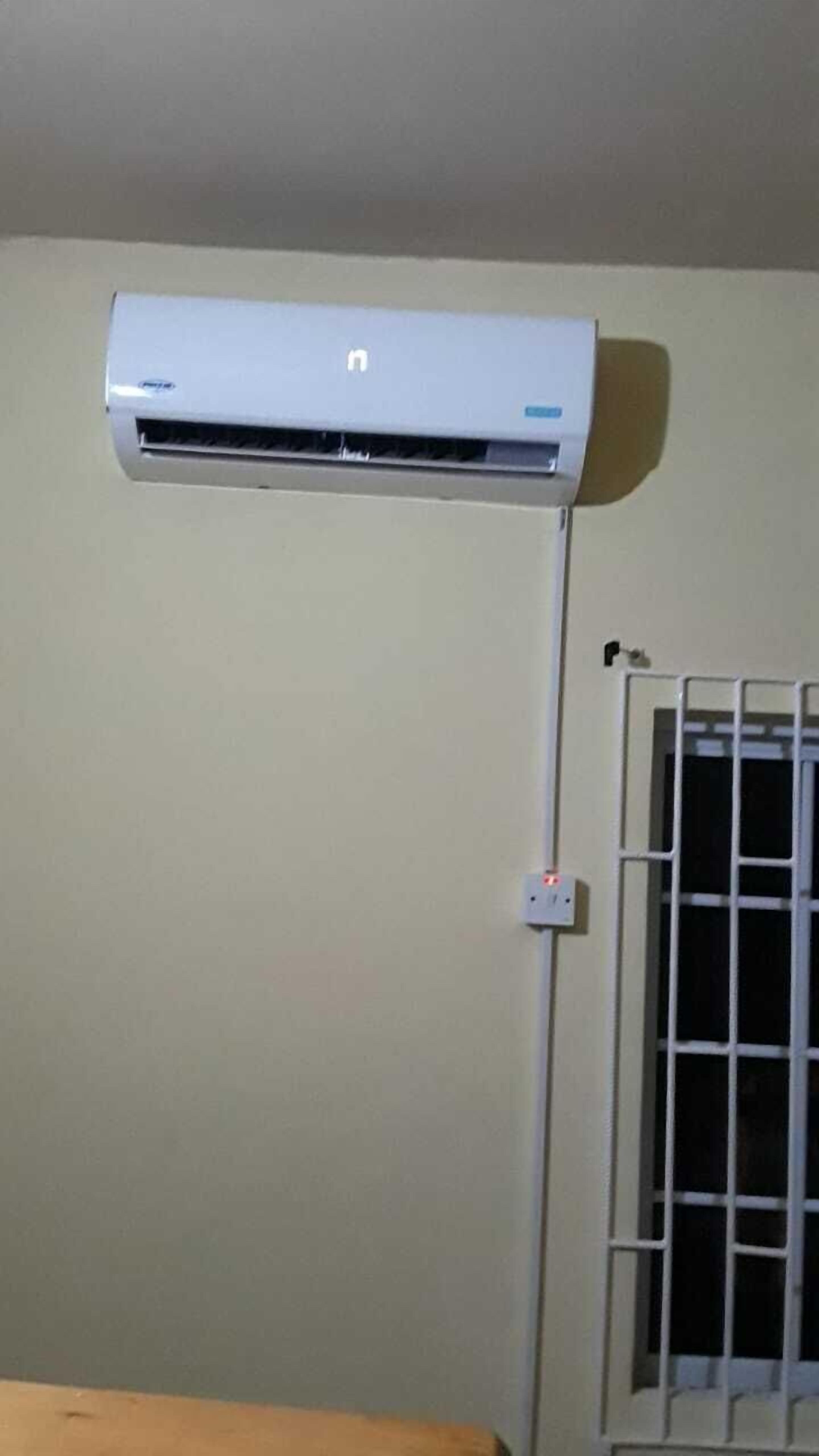 Un equipo de aire acondicionado blanco montado en una pared, con una celosía de ventana a la derecha.