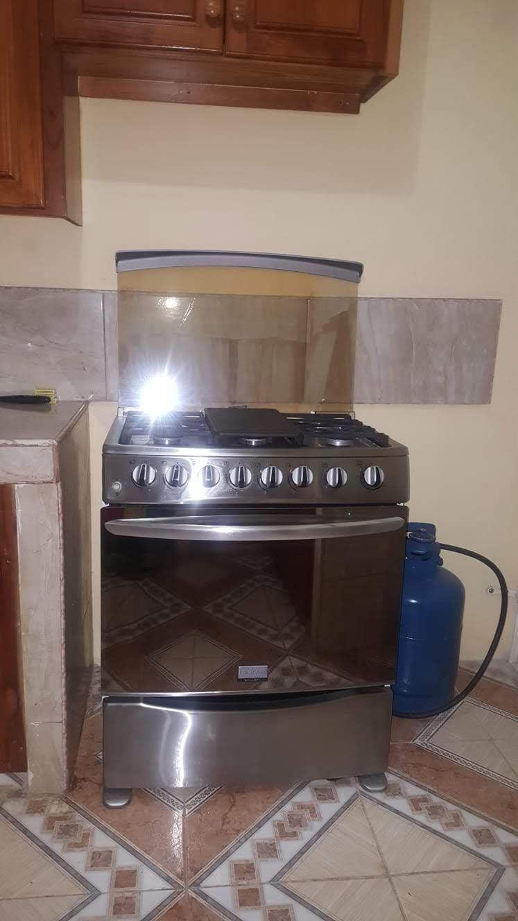 Une cuisine équipée d’une cuisinière et d’un four à gaz, d’une bouteille de gaz bleue et d’un sol carrelé.