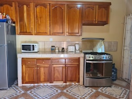 Una cocina con armarios de madera, microondas, tostadora, cafetera, cocina a gas y refrigerador.