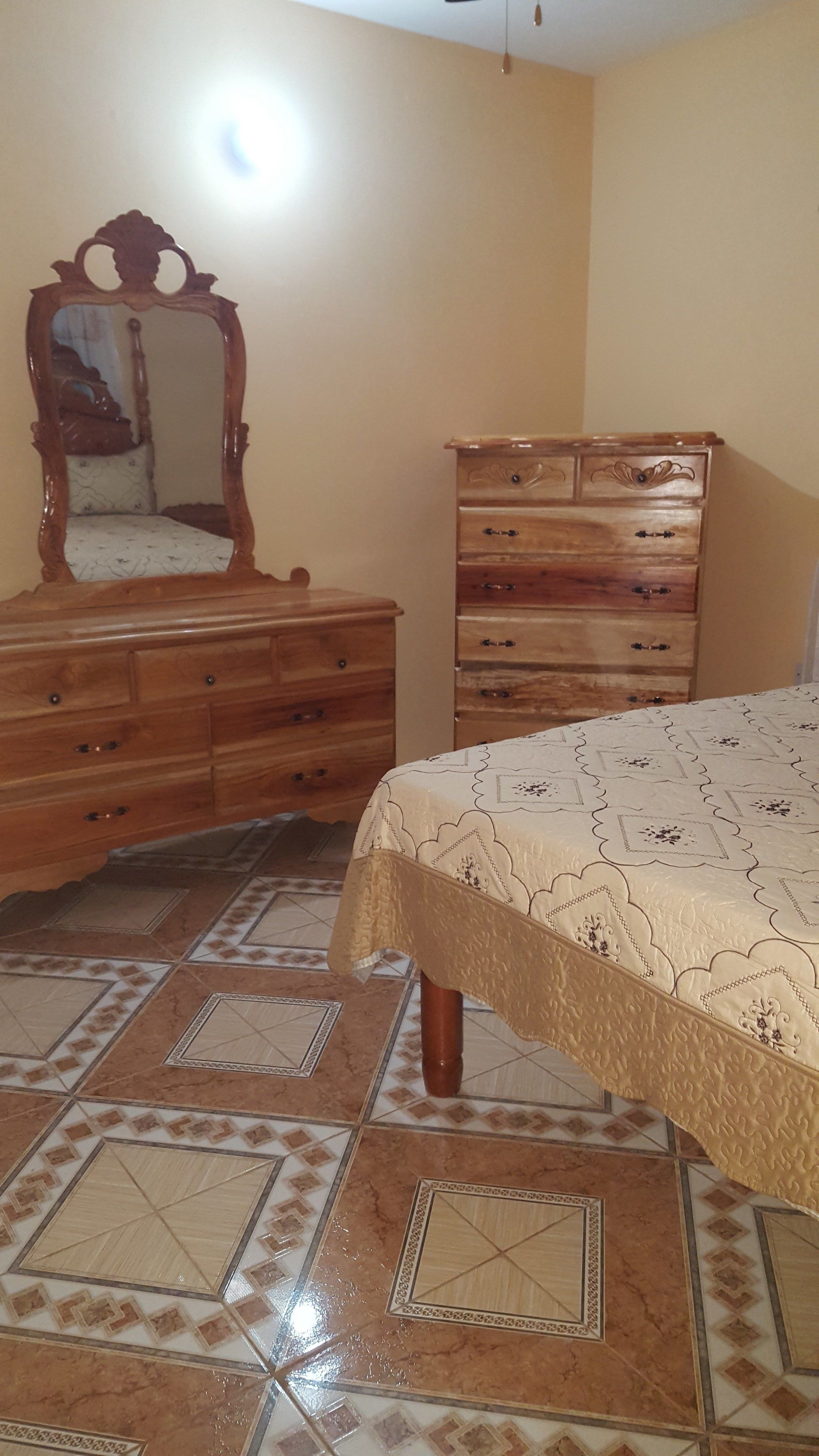 Un dormitorio con cama, cómoda, espejo y piso de baldosas.