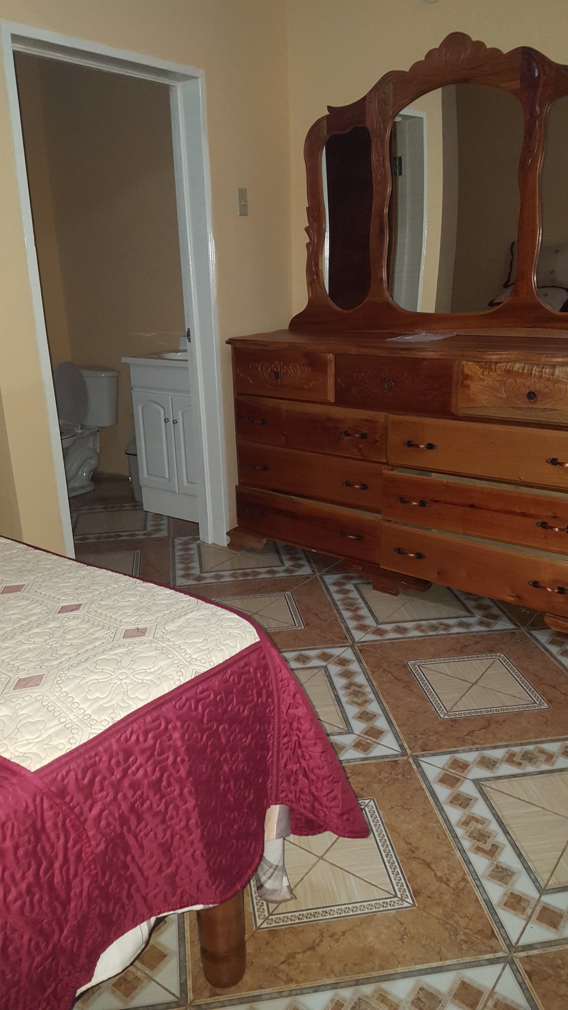 A bedroom with a bed, a wooden dresser with a mirror, and a bathroom visible through an open door.