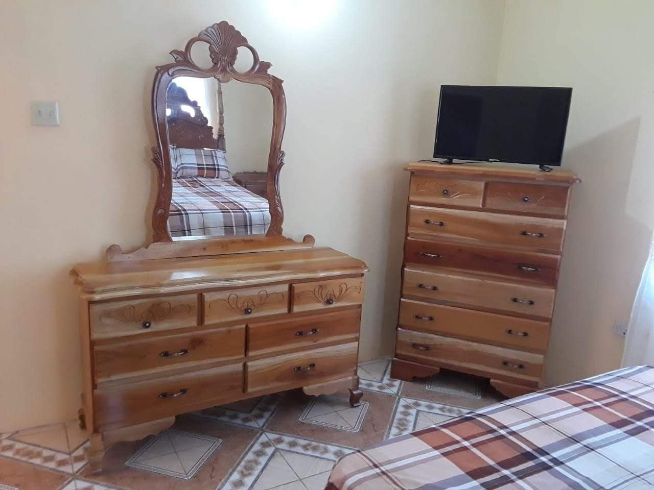 A bedroom with a bed, a wooden dresser with drawers, a television on top, and a mirror above the dresser.