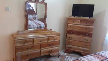 A bedroom with a bed, a wooden dresser with drawers, a television on top, and a mirror above the dresser.