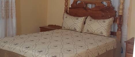 Un dormitorio con estructura de cama de madera, colcha estampada y ventilador de techo.