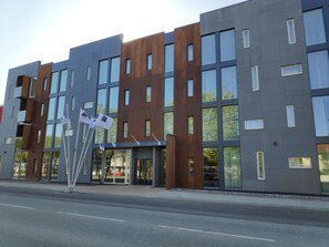Un edificio moderno de varios pisos con fachadas de vidrio y metal, que destaca por una entrada principal con puerta de cristal y un cartel.