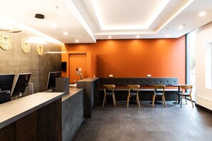 Una zona de recepción moderna con mostrador, computadoras, un espacio de asientos con banca y un ventanal grande.