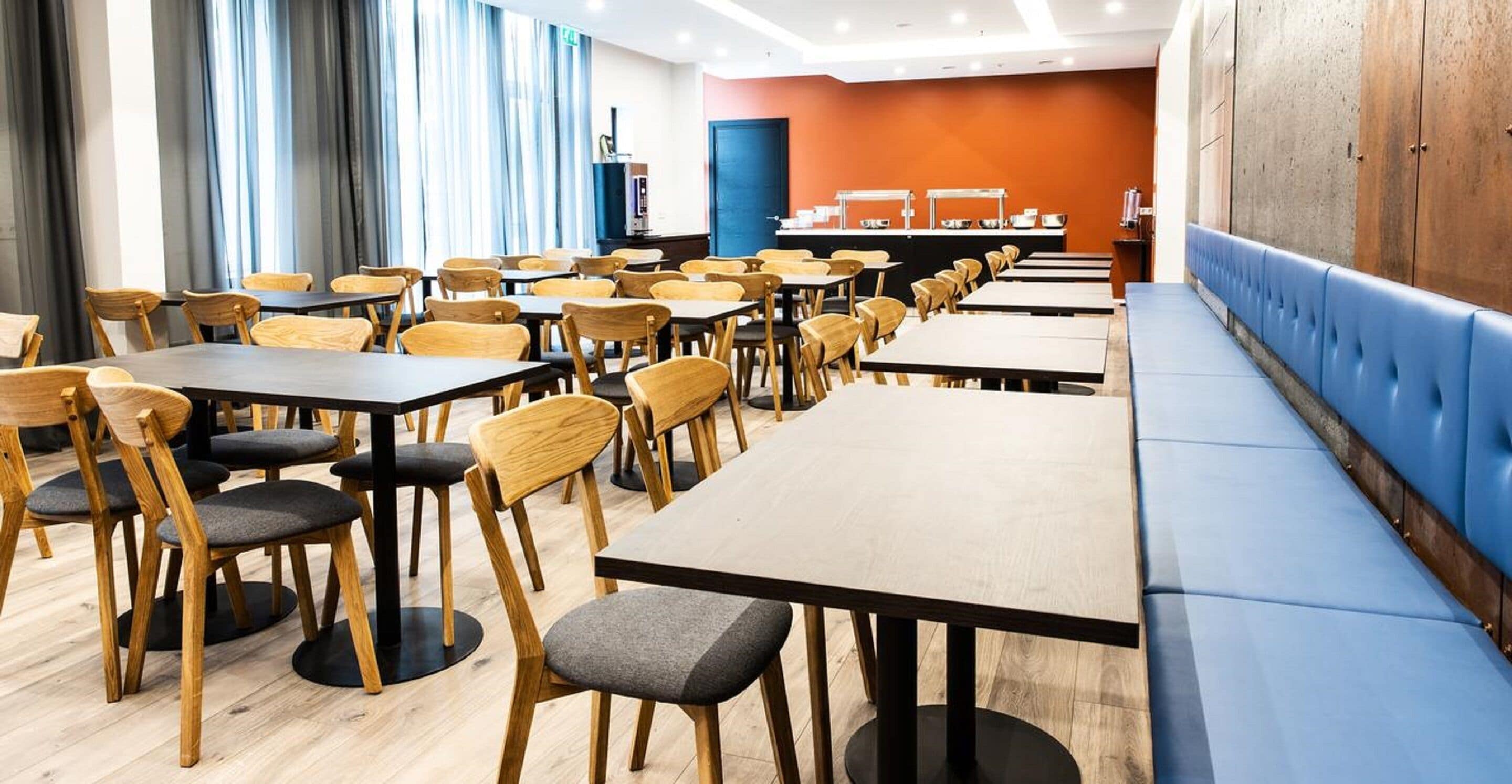 Een moderne eetruimte met houten tafels en stoelen, een blauwe met kussens beklede bank en een buffet in de achtergrond.