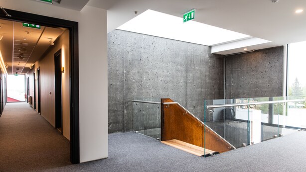 A modern interior with a long hallway, a staircase with glass railings, and a skylight. - Hotel South Coast (Selfoss)