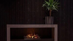 A modern outdoor seating area with a fireplace, dark wooden walls, and a potted plant. - Hotel South Coast (Selfoss)