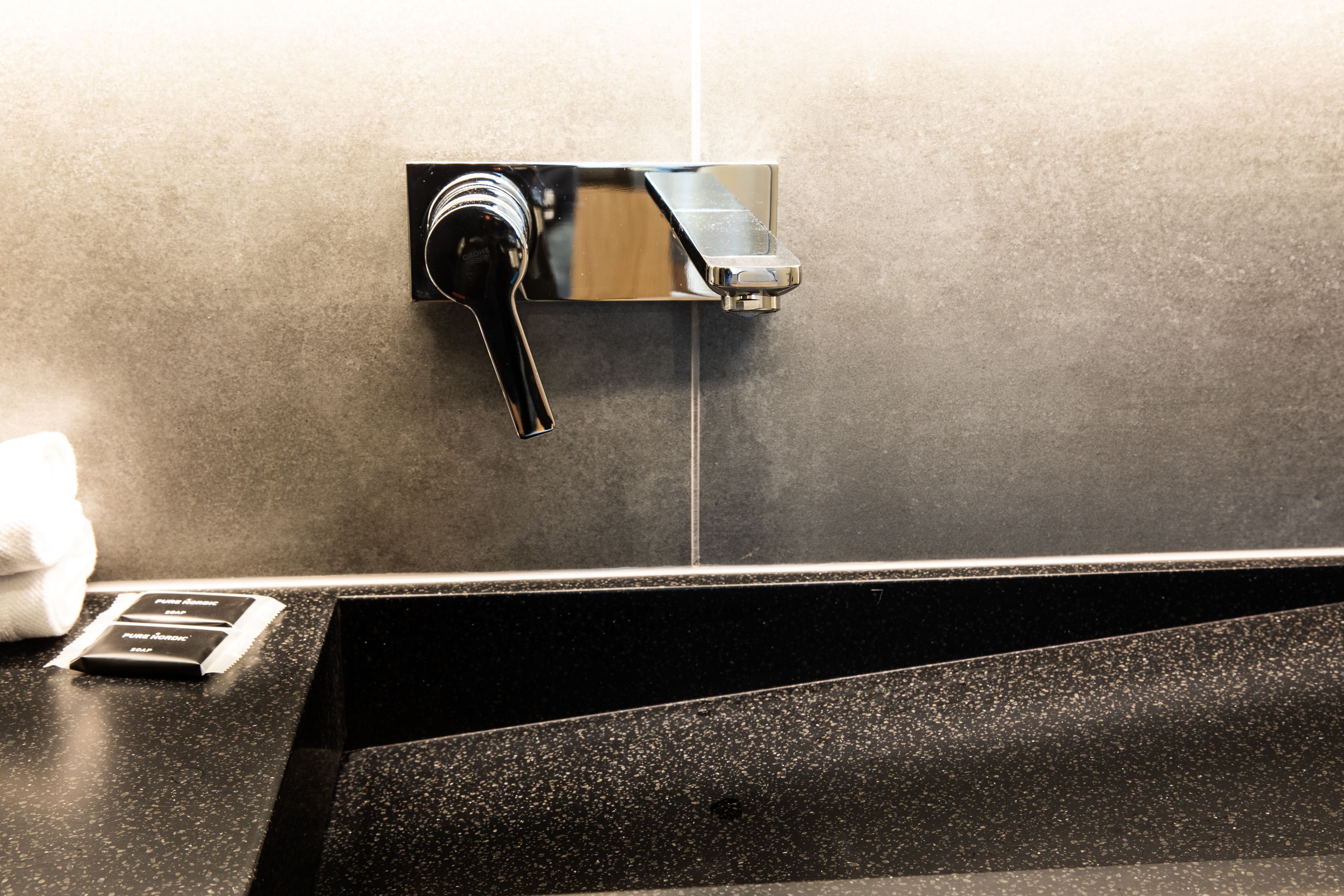 Une salle de bain moderne avec un plan de toilette noir, un robinet chromé et un distributeur de serviettes.
