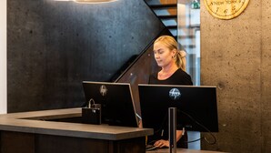 A reception desk with two HP computers, a clock displaying 'NEW YORK', and a modern interior with a concrete wall and a staircase. - Hotel South Coast (Selfoss)